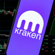 A phone with the kraken logo in front of a screen bearing financial data